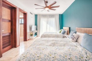 Ein Schlafzimmer mit zwei Betten, einem Deckenventilator, einem Fernseher und einem Fenster mit Vorhängen.