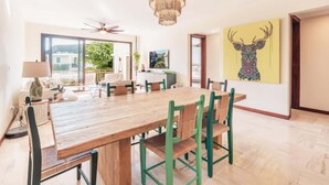 A dining area with a wooden table and green chairs, a chandelier, and a large painting of a deer on the wall. - Comfortable apt with 2br w balcony in Portillo (Las Terrenas)