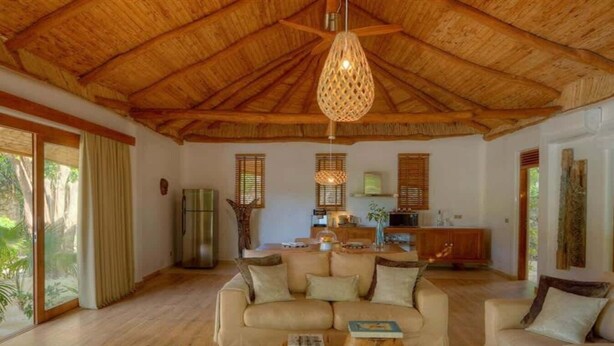 A spacious living area with a high wooden ceiling, a sofa set, a coffee table, and a kitchen in the background. - Zanzibar Family Paradise Villa (Paje)