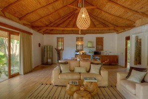 A spacious living area with a high wooden ceiling, a sofa set, a coffee table, and a kitchen in the background. - Zanzibar Family Paradise Villa (Paje)