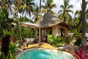 Ein tropisches Resort mit Pool, Palmen und einer strohgedeckten Hütte.