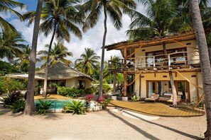 Ein Resort mit zwei Etagen, einem Pool, Palmen und einem Gebäude mit einem Reetdach.