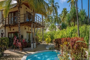 A pool surrounded by tropical vegetation and a multi-story building with balconies. - Zanzibar Family Paradise Villa (Paje)