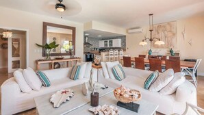 A spacious living room with a large white sofa, a coffee table, and a dining area with a wooden table and chairs. - Villa with ocean view bbq pool resort access (Sánchez)
