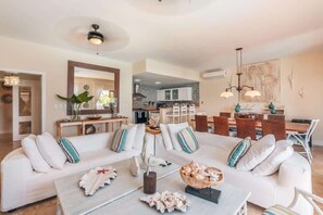 Ein geräumiges Wohnzimmer mit einem großen weißen Sofa, einem Couchtisch und einem Essbereich mit Holztisch und Stühlen.