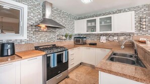 A modern kitchen with white cabinets, a stainless steel range hood, a microwave, and a double sink. - Villa with ocean view bbq pool resort access (Sánchez)