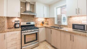 Cozinha moderna com bancadas de granito, eletrodomésticos de aço inoxidável e armários brancos.