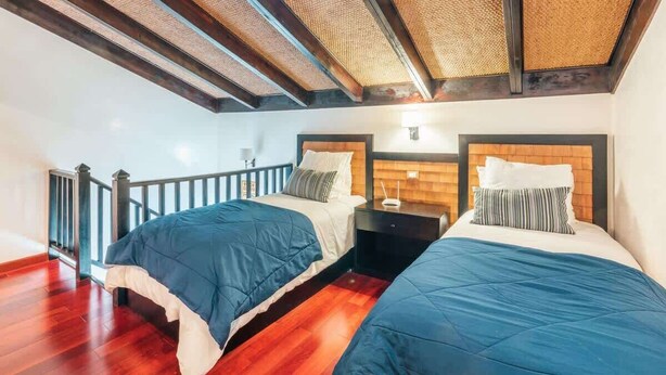 Quarto com duas camas, soalho de madeira, varanda e teto de vime.