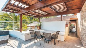 Um alpendre coberto com mesa e cadeiras, vista para a paisagem ao redor e um caminho que leva a um edifício.