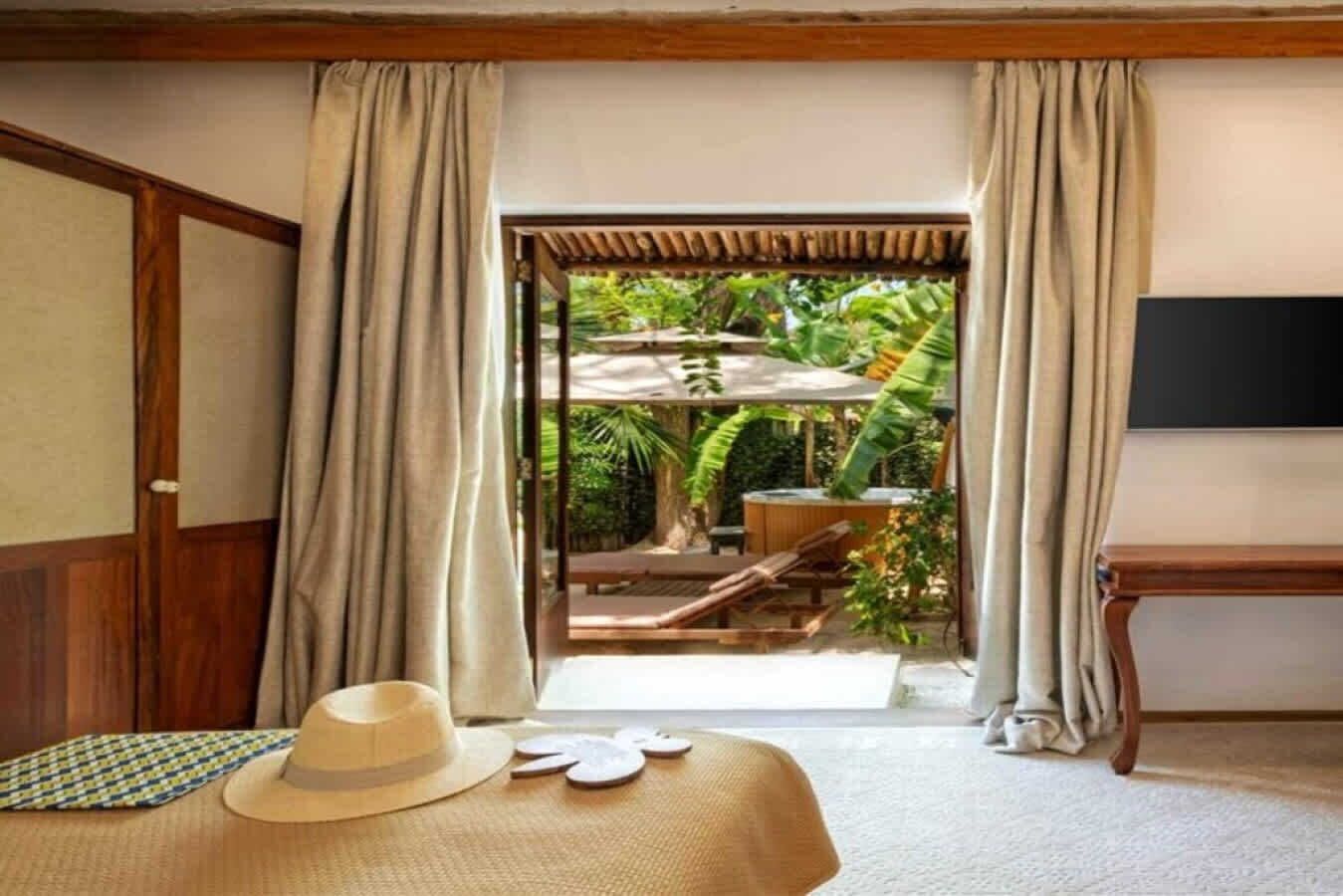 Quarto com cama, televisão e vista para área externa com hidromassagem e cadeiras de lounge.
