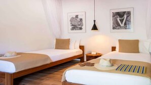 Habitación de hotel con dos camas individuales, una mesita de noche, una lámpara y obras de arte en las paredes.