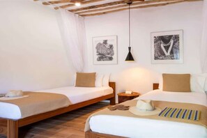 A hotel room with two single beds, a nightstand, a lamp, and artwork on the walls. - Spice Route Family Room (Paje)