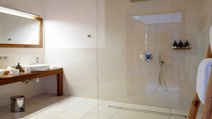 Un baño moderno con ducha envuelta en vidrio, tocador de madera con lavamanos y un espejo sobre el tocador.