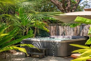A hot tub in a garden with a bamboo fence, surrounded by tropical plants. - Spice Route Family Room (Paje)