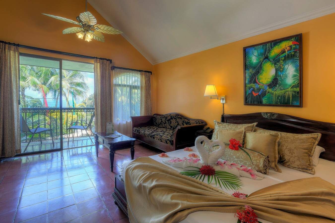 A hotel room with a balcony, a bed with floral decorations, a sofa, and a painting on the wall.