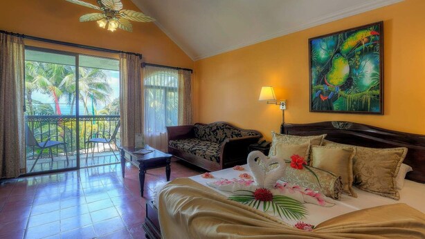 A hotel room with a balcony, a bed with floral decorations, a sofa, and a painting on the wall.