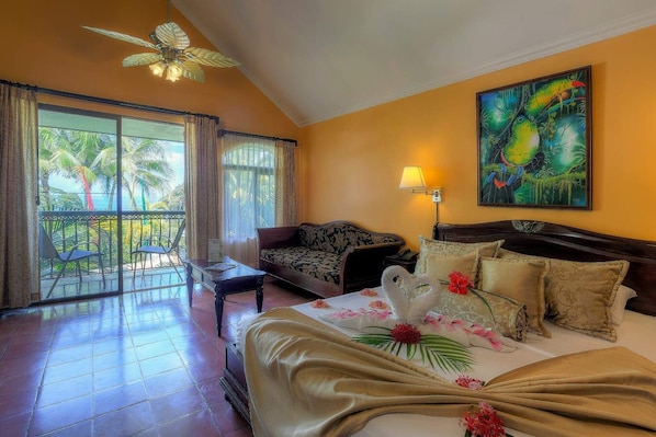 A hotel room with a balcony, a bed with floral decorations, a sofa, and a painting on the wall.