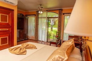 A hotel room with a bed, curtains, a ceiling fan, and a view of a garden.