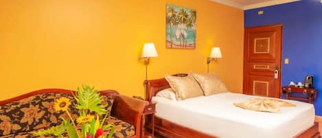 A hotel room with a bed, a sofa, two wall-mounted lamps, a painting, and a door.