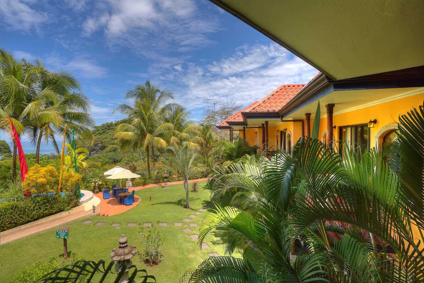 Um jardim tropical com palmeiras, um gazebo e um edifício com telhado vermelho.