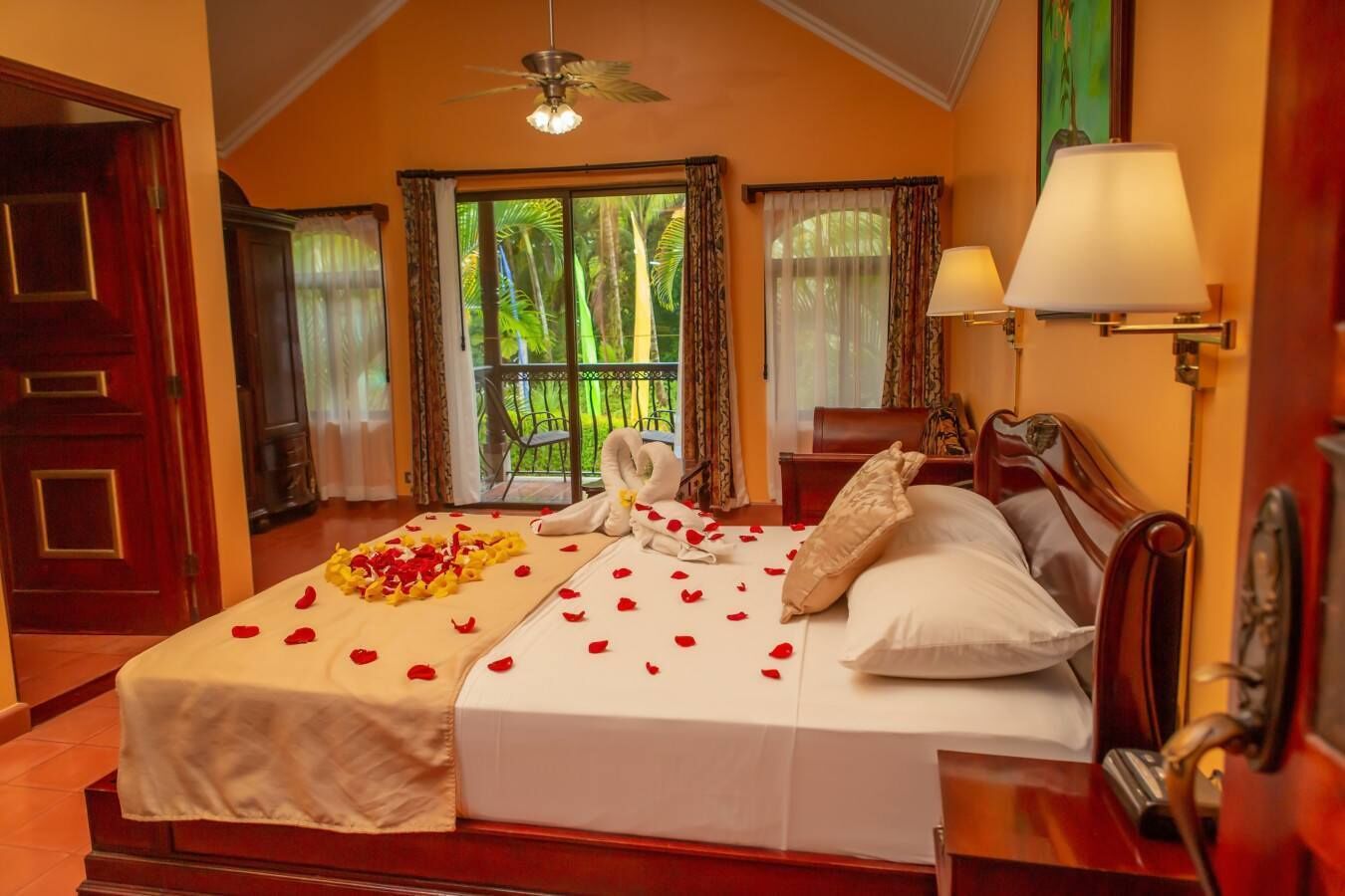 A hotel room with a bed, a nightstand, a lamp, and a view of greenery outside.