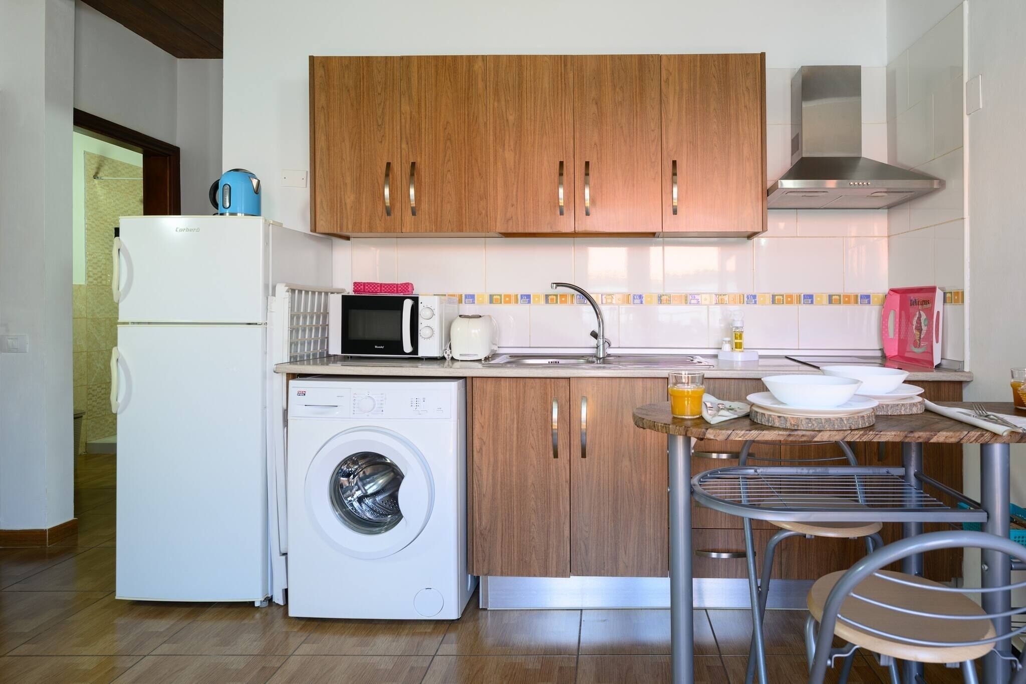 A compact kitchen with wooden cabinets, a washing machine, a microwave, and a sink.