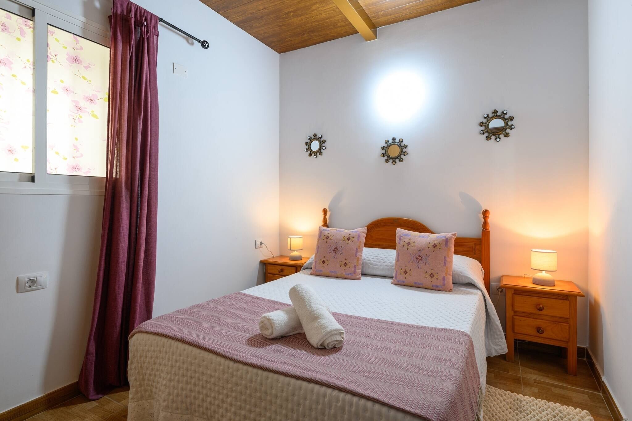 A bedroom with a bed, two bedside tables, a nightstand, a window with curtains, and wall-mounted decor.