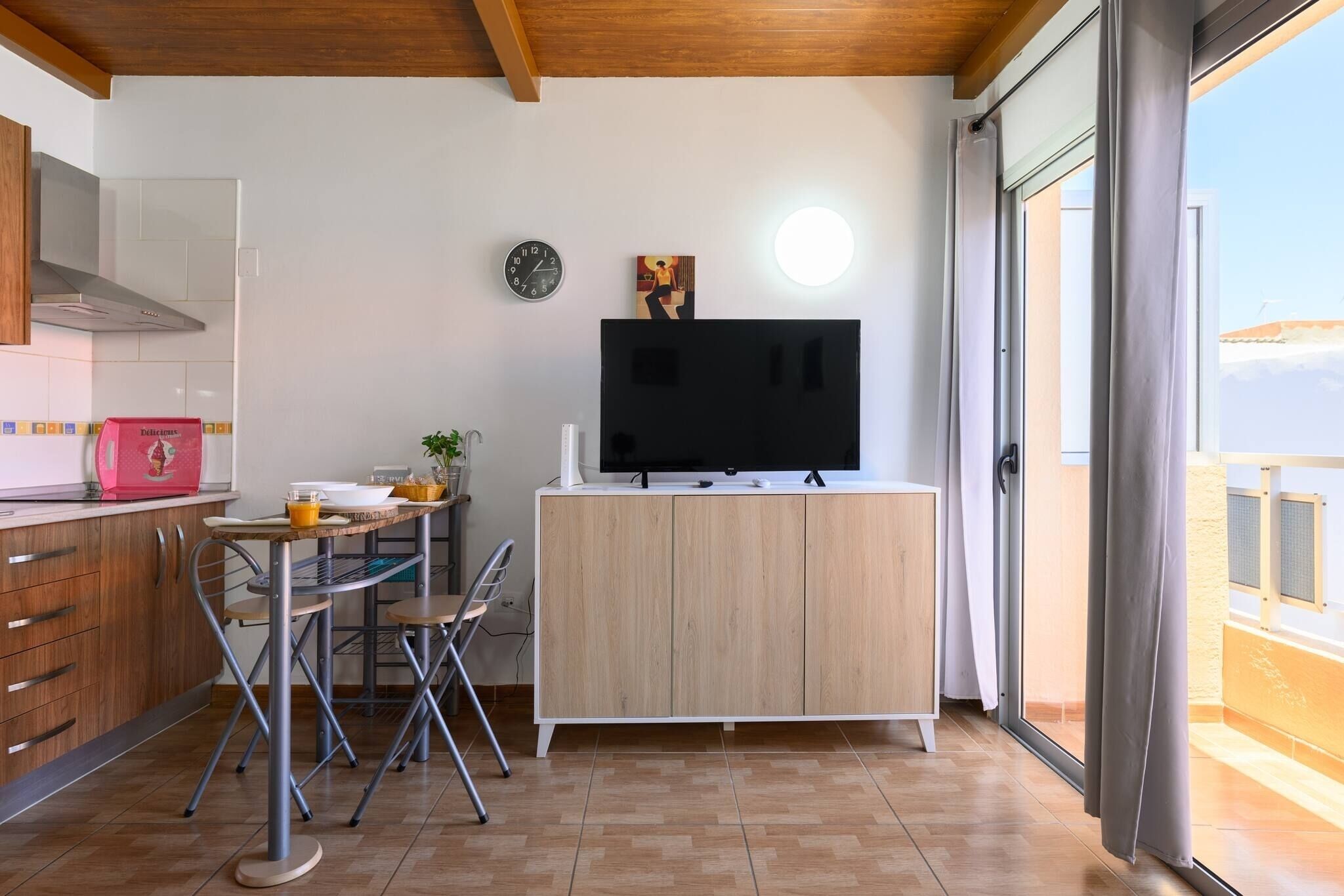 A modern kitchen with a dining area, a TV on a cabinet, and a view of the outdoors.
