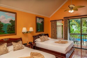 A hotel room with two beds, a balcony with a view of greenery, and a ceiling fan.