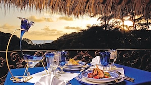 A table set for a meal with a view of the sunset, featuring blue glassware and plates with food. - Rainforest Family Angel Suite (Bahía Ballena)