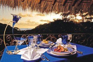 A table set for a meal with a view of the sunset, featuring blue glassware and plates with food.