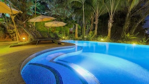 A swimming pool with a curved design, surrounded by palm trees and outdoor seating with umbrellas. - Rainforest Family Angel Suite (Bahía Ballena)