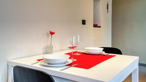 Una mesa de comedor dispuesta con platos blancos, servilletas rojas y copas de vino transparentes, con una rosa roja en un florero de vidrio.