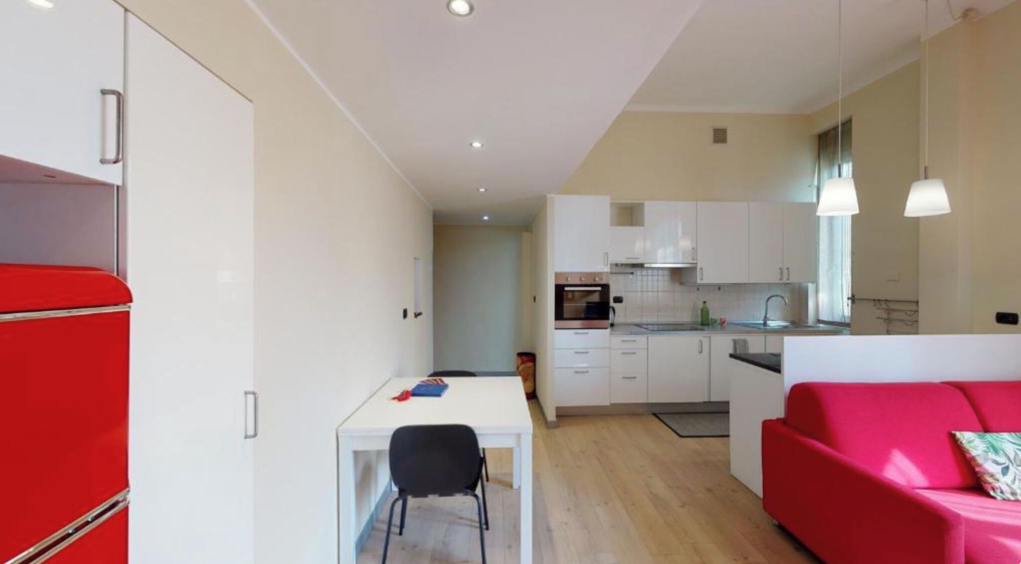 A compact living space with a kitchenette, a dining area, and a red sofa.