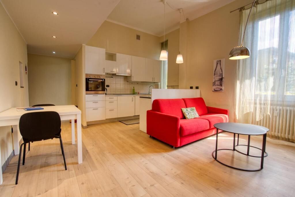 A modern living room with a red sofa, a small round table, and a white dining table with a black chair.