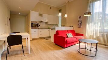 A modern living room with a red sofa, a small round table, and a white dining table with a black chair.