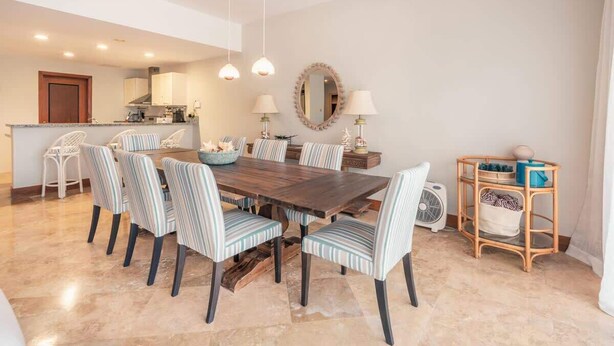 A dining area with a wooden table and striped chairs, a kitchen in the background, and a mirror on the wall. - 3br 10 guests ocean view  Bbq in Samana (Sánchez)