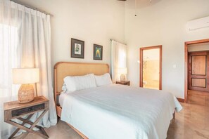 A bedroom with a large bed, two bedside tables, a wooden door, and a wall-mounted air conditioning unit. - 3br 10 guests ocean view  Bbq in Samana (Sánchez)