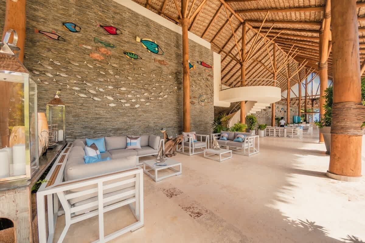 A spacious lobby with a stone wall, a thatched roof, and a seating area with sofas and tables.