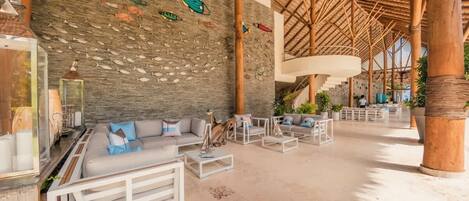 A spacious lobby with a stone wall, a thatched roof, and a seating area with sofas and tables.