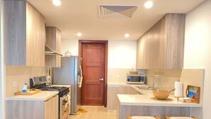 A modern kitchen with wooden cabinets, a stove, a microwave, and two bar stools. - Charming two-bedroom apartment in Portillo (Las Terrenas)