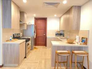 A modern kitchen with wooden cabinets, a stove, a microwave, and two bar stools. - Charming two-bedroom apartment in Portillo (Las Terrenas)