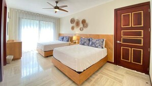 A hotel room with two beds, a ceiling fan, a wooden door, and a bedside table with a lamp. - Charming two-bedroom apartment in Portillo (Las Terrenas)