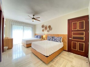 A hotel room with two beds, a ceiling fan, a wooden door, and a bedside table with a lamp. - Charming two-bedroom apartment in Portillo (Las Terrenas)