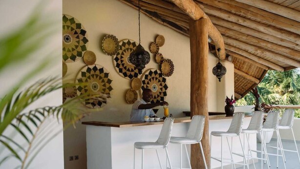 A bar area with a wooden ceiling, a white counter, and several white chairs. - Spice Route Double Room (Paje)