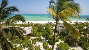A beach resort with thatched-roof huts, palm trees, and a view of the ocean. - Spice Route Double Room (Paje)