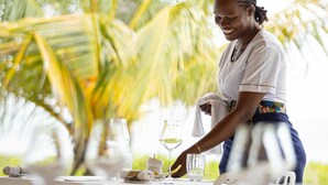 A person setting up a table with glassware and a folded napkin, palm trees in the background, and a clear sky. - Spice Route Double Room (Paje)