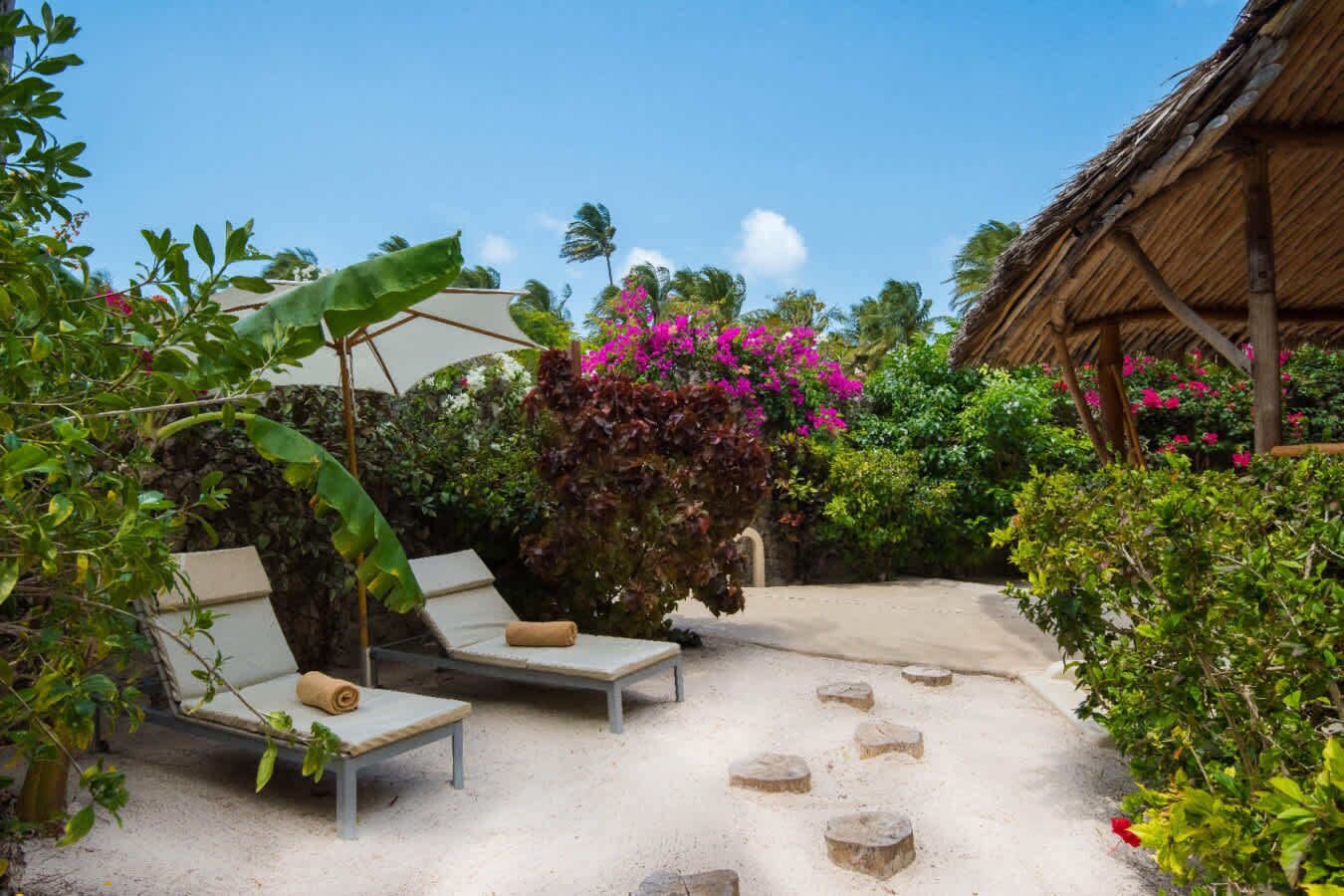 A tropical outdoor seating area with lounge chairs and a thatched-roof structure.