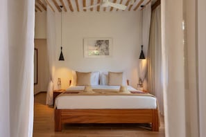 A hotel room with a wooden bed, white bedding, a painting on the wall, and two pendant lights. - Spice Route Double Room (Paje)