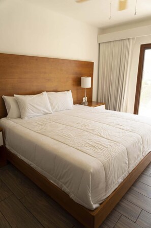 Un letto grande con testiera in legno, biancheria da letto bianca e un comodino con una lampada.